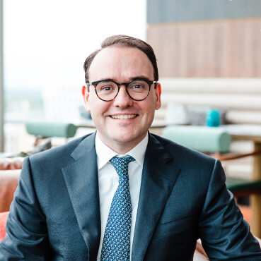 Bas-Sluijsmans A smiling man wearing glasses in a blue suit and tie.