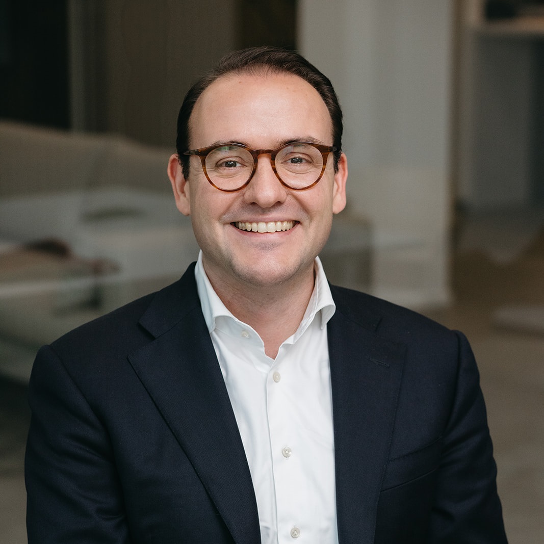 A smiling man wearing glasses in a blue suit and tie.
