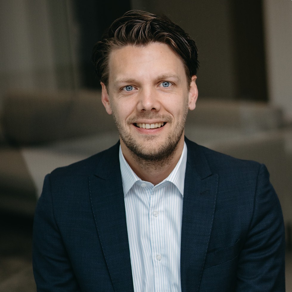A smiling man wearing glasses in a blue suit and tie.